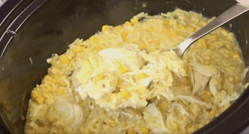 A spoonful of cheesy chicken and rice in the crockpot