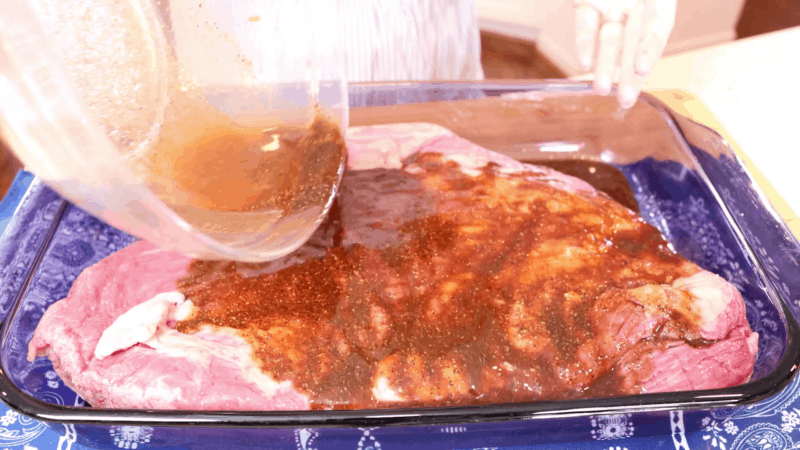 Pouring marinade over beef brisket in baking dish.