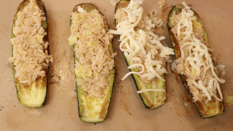 Rice-stuffed zucchini boats being topped with cheese.