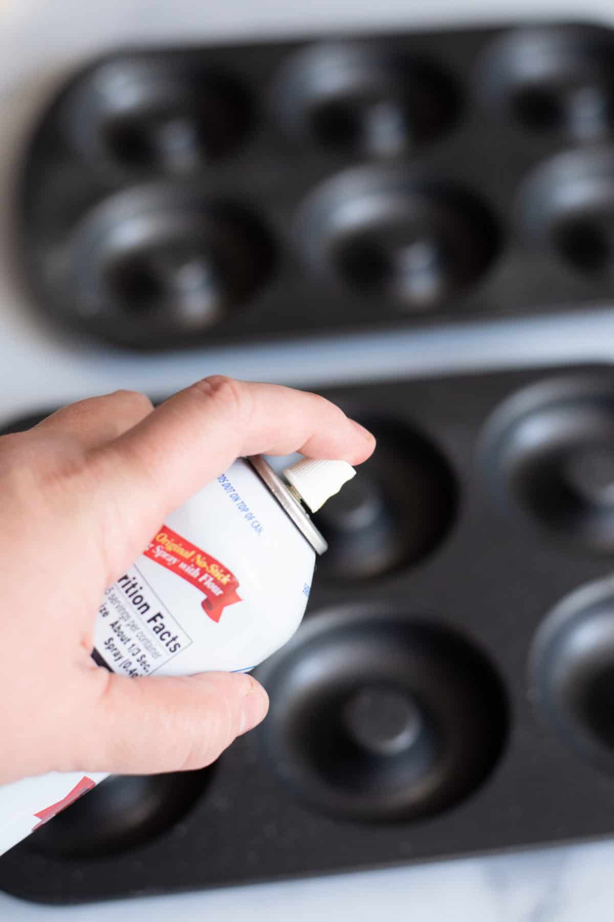 Spraying oil into donut pan.