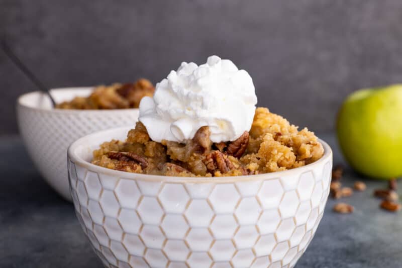 Apple crumble in bowl with whipped cream on top.
