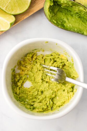 Mashing avocado in small bowl with fork.