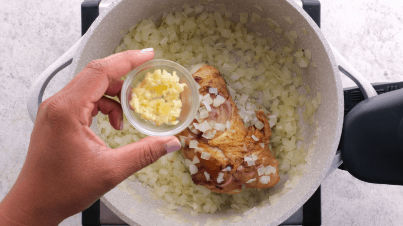 Adding garlic to onion and ham hock in pot.