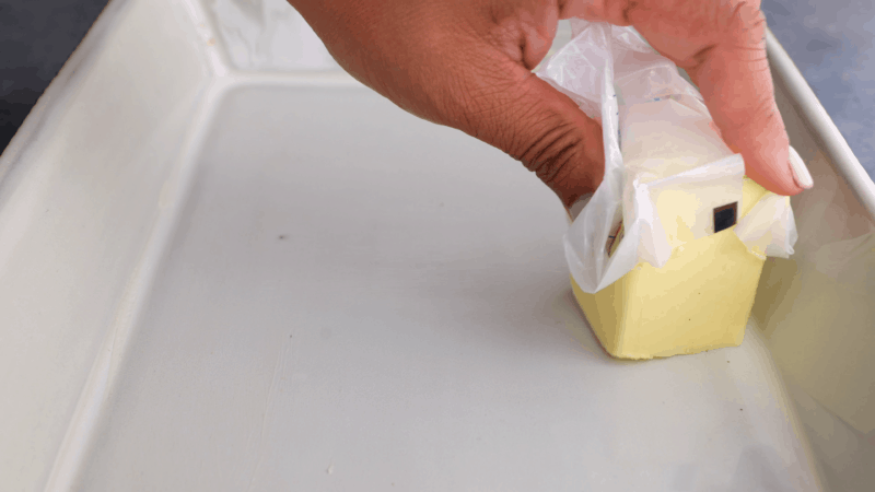 Spreading stick of butter over dish.
