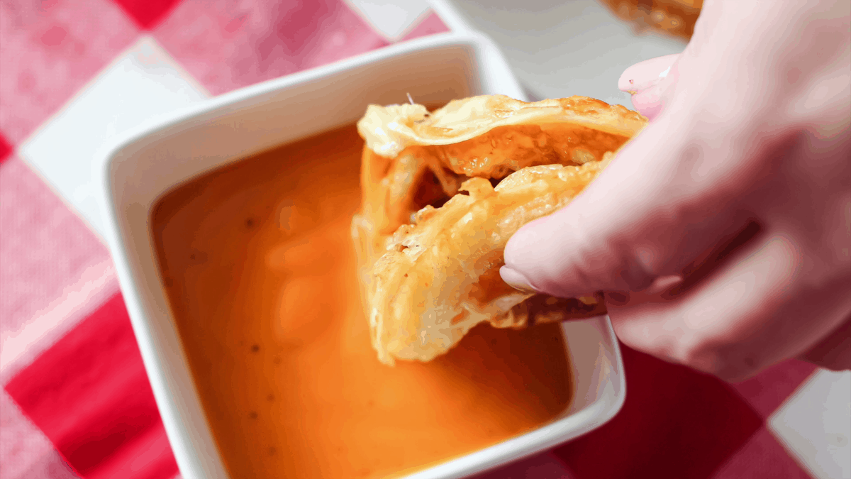 Dipping keto chaffle with onion ring in sauce.