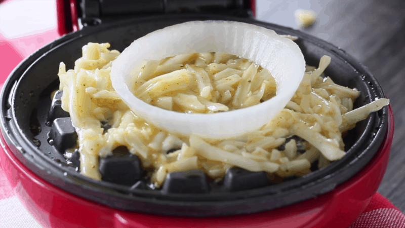 Onion ring on top of batter in waffle maker.