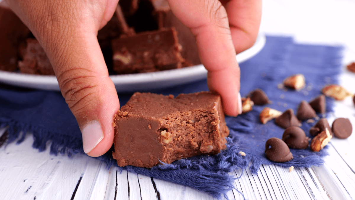 Hand holding piece of chocolate fudge with bite removed.