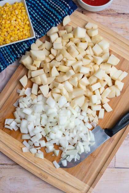 Peeled and diced potatoes and onions on a wooden cutting board.