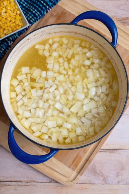 Diced potatoes and onions in a Dutch oven with reserved chicken broth.