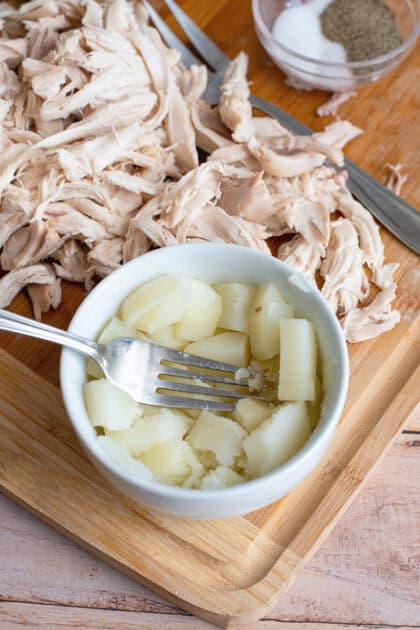 A fork mashing potato in a small white dish.