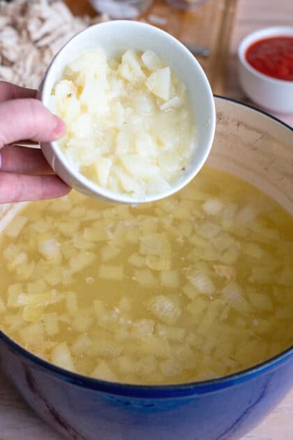 Adding mashed potatoes to pot of broth and diced onions.