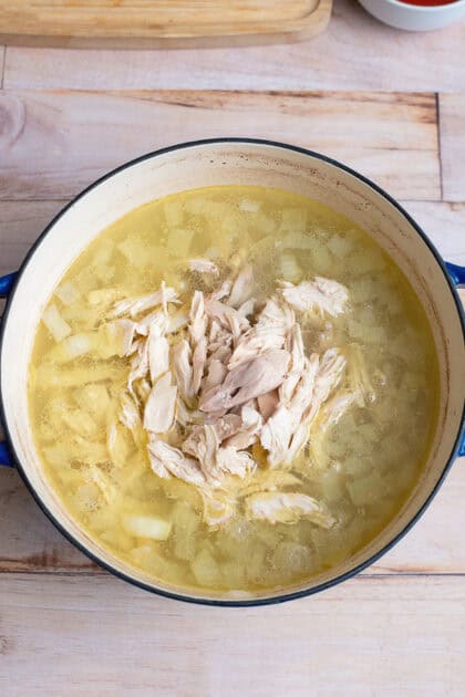 Shredded chicken in a pot of broth and diced onion.