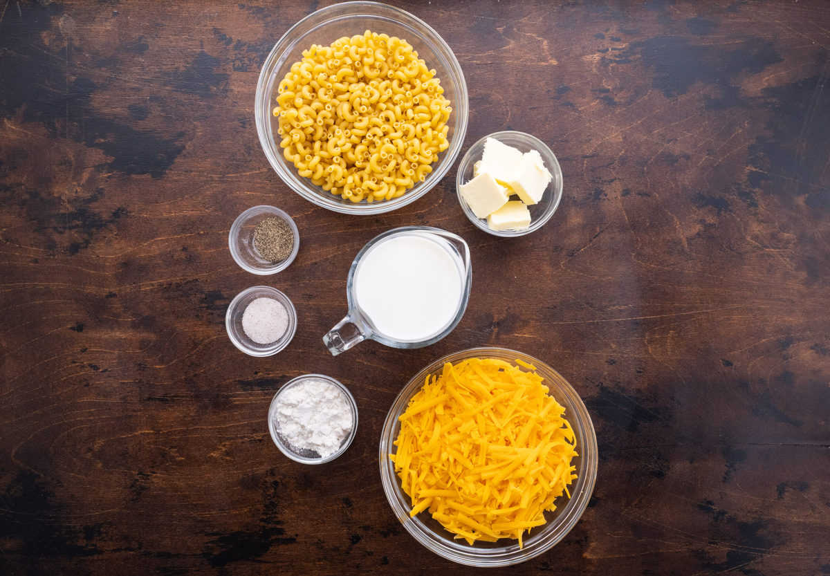Ingredients for oven-baked mac and cheese, featuring cheddar cheese, flour, macaroni pasta, butter, milk, salt, and pepper.