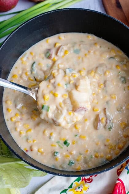 A spoon taking a scoop out of a pot of corn chowder.