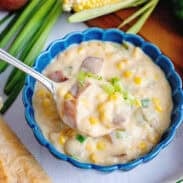 A spoon scooping potato corn chowder in a blue bowl.