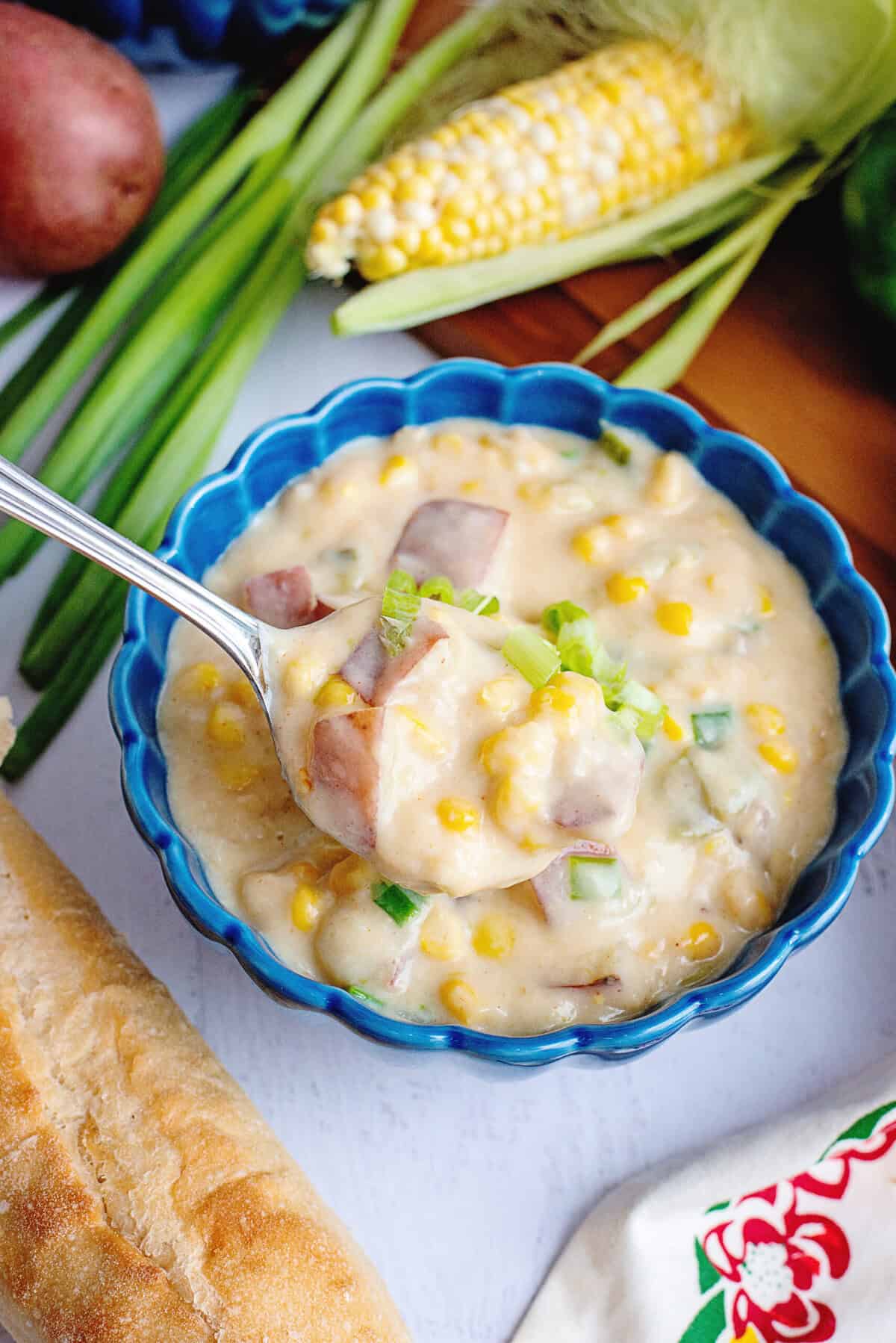 A spoon scooping potato corn chowder in a blue bowl.