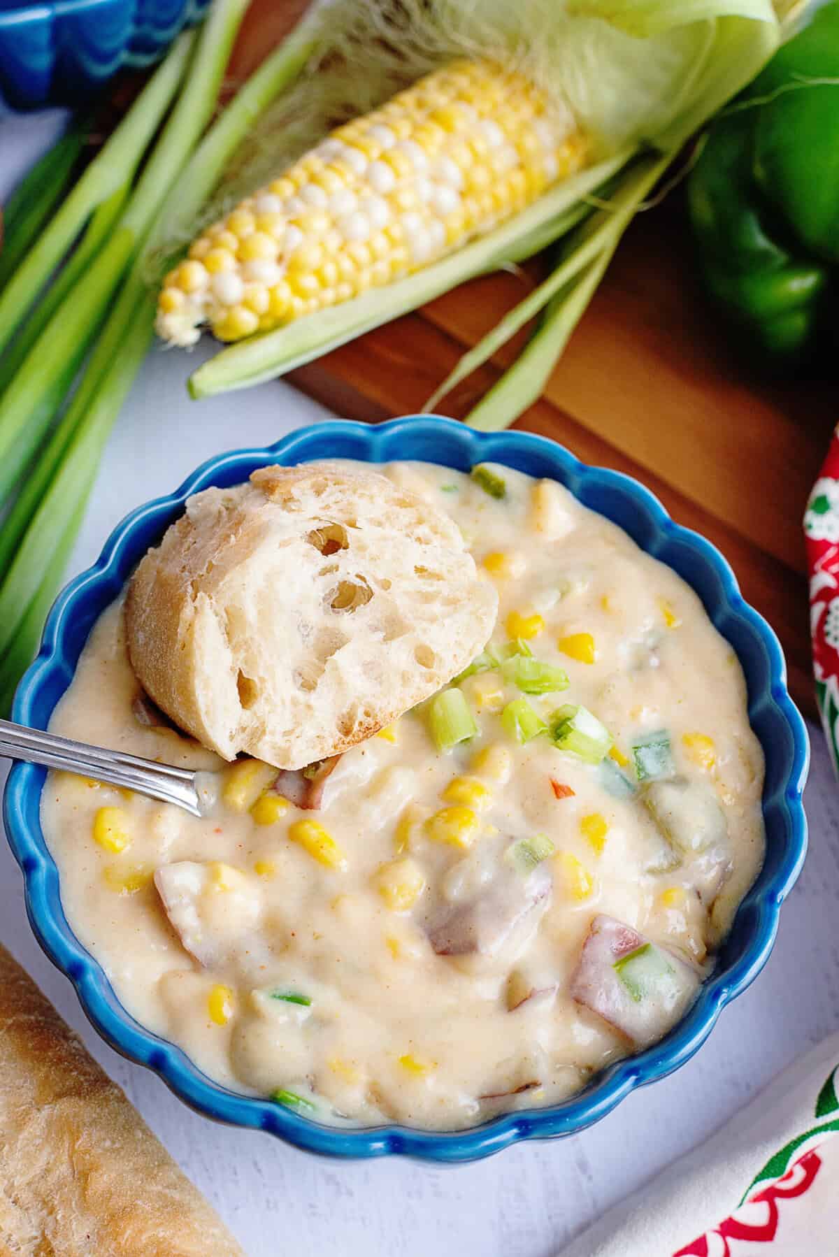 Corn chowder in a blue bowl with a piece of bread on the side.