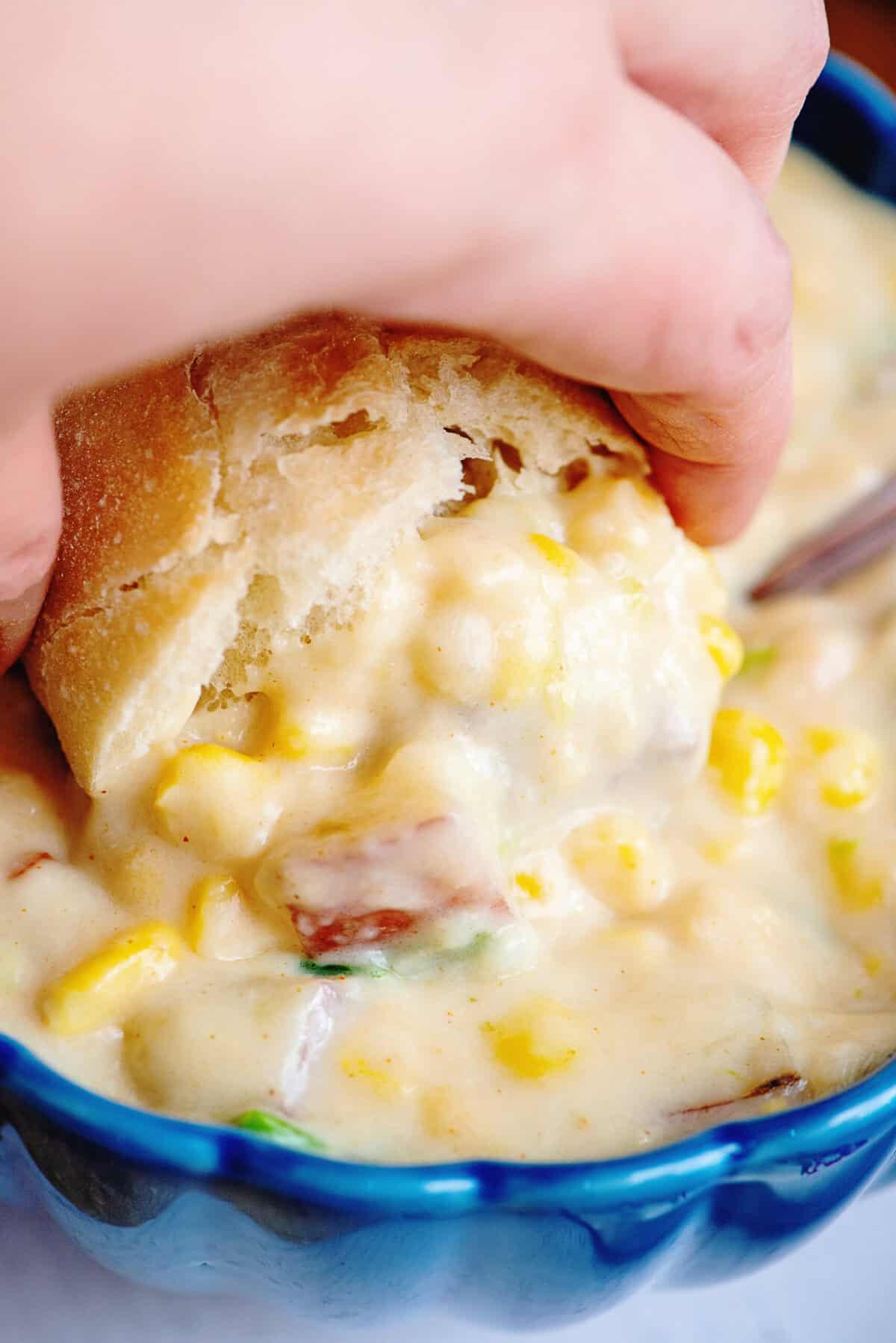 Dipping crusty bread into a bowl of potato corn chowder.