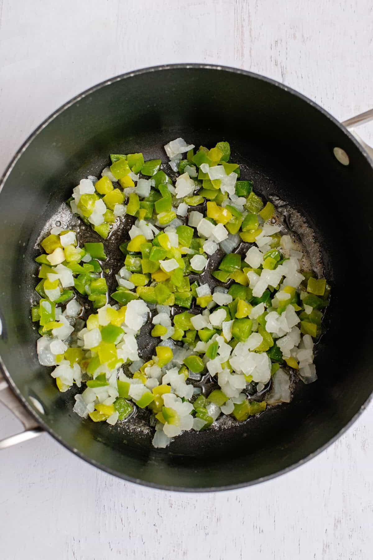 Onion and green bell pepper sautéing in a pan.