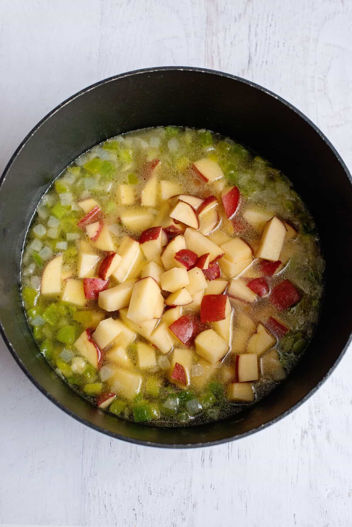 Chopped red potatoes in a pan with broth, onions, and green bell peppers.