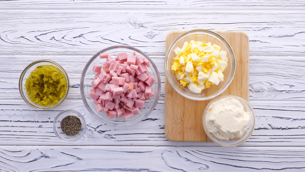 Ingredients for old-fashioned ham salad sandwich recipe, featuring spicy brown mustard, sweet pickle relish, mayonnaise, boiled eggs, black pepper, and chopped ham.