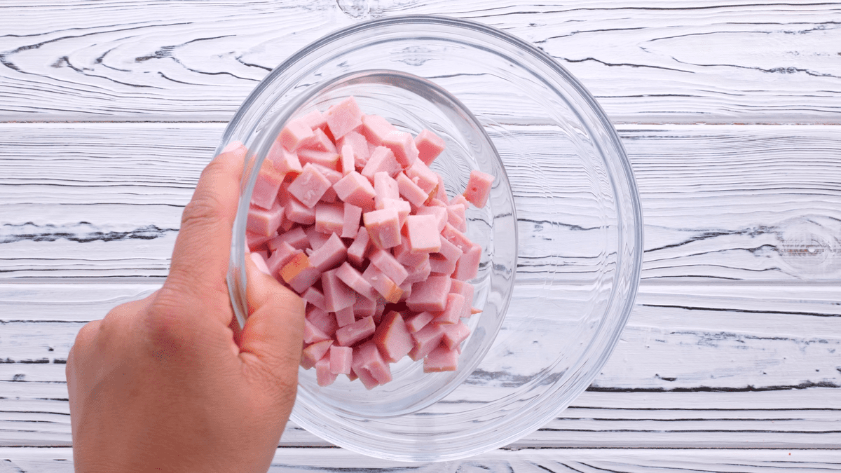 A hand holding chopped ham in a mixing bowl.