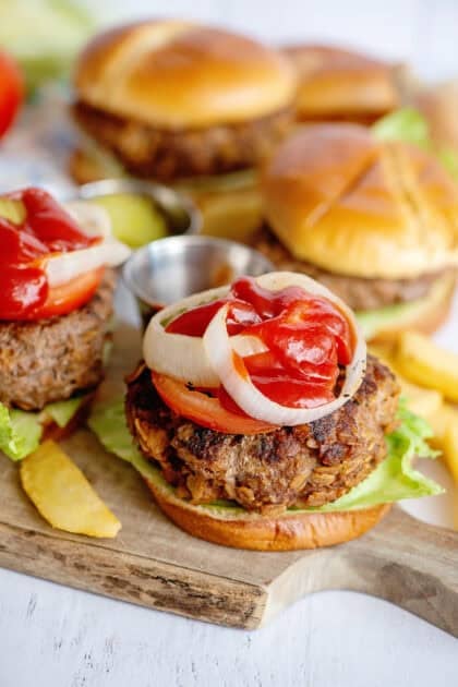 Topping meatloaf burgers with tomato, onion, and ketchup.