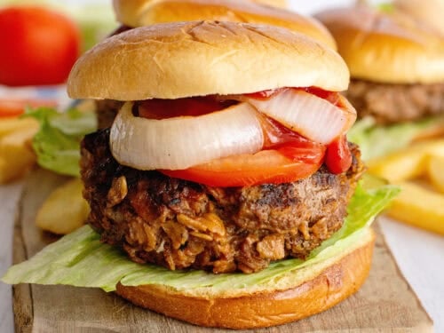 Meatloaf burgers on a wooden serving tray with onion, tomato, and lettuce.