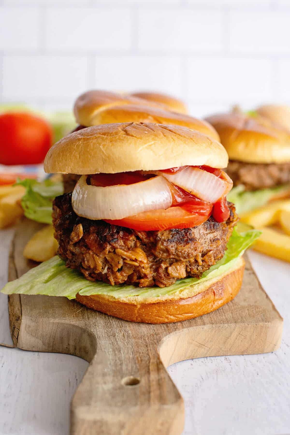 Meatloaf burgers on a wooden serving tray with onion, tomato, and lettuce.