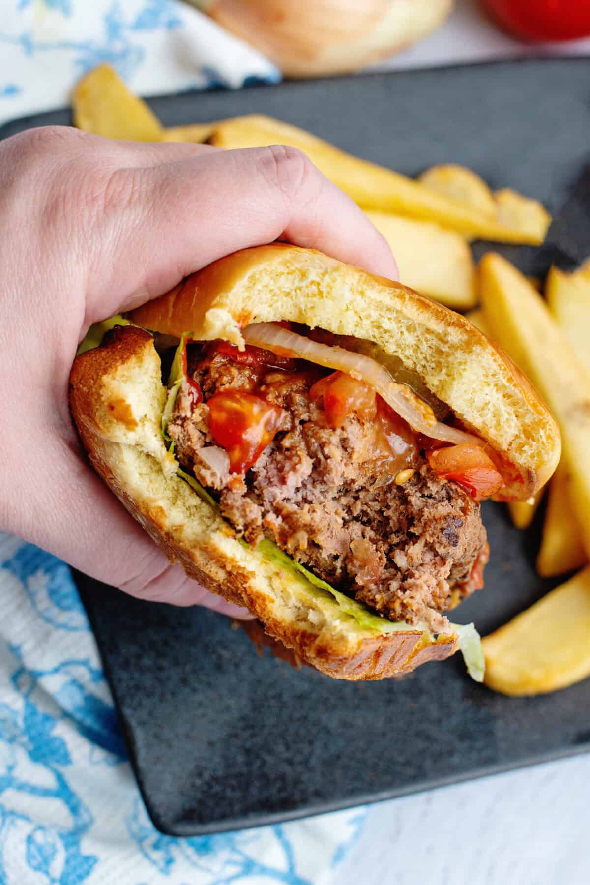 A hand grabbing a meatloaf burger ready to take another bite!