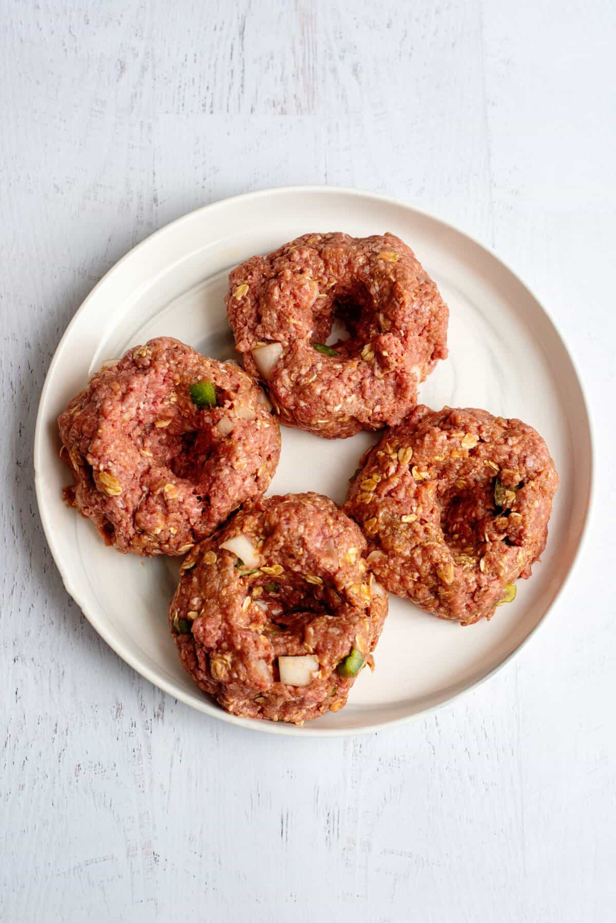 Doughnut-shaped meatloaf patties on a white plate ready to pan-fry.