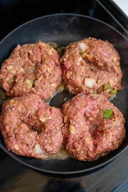 Raw meatloaf patties searing in a pan.
