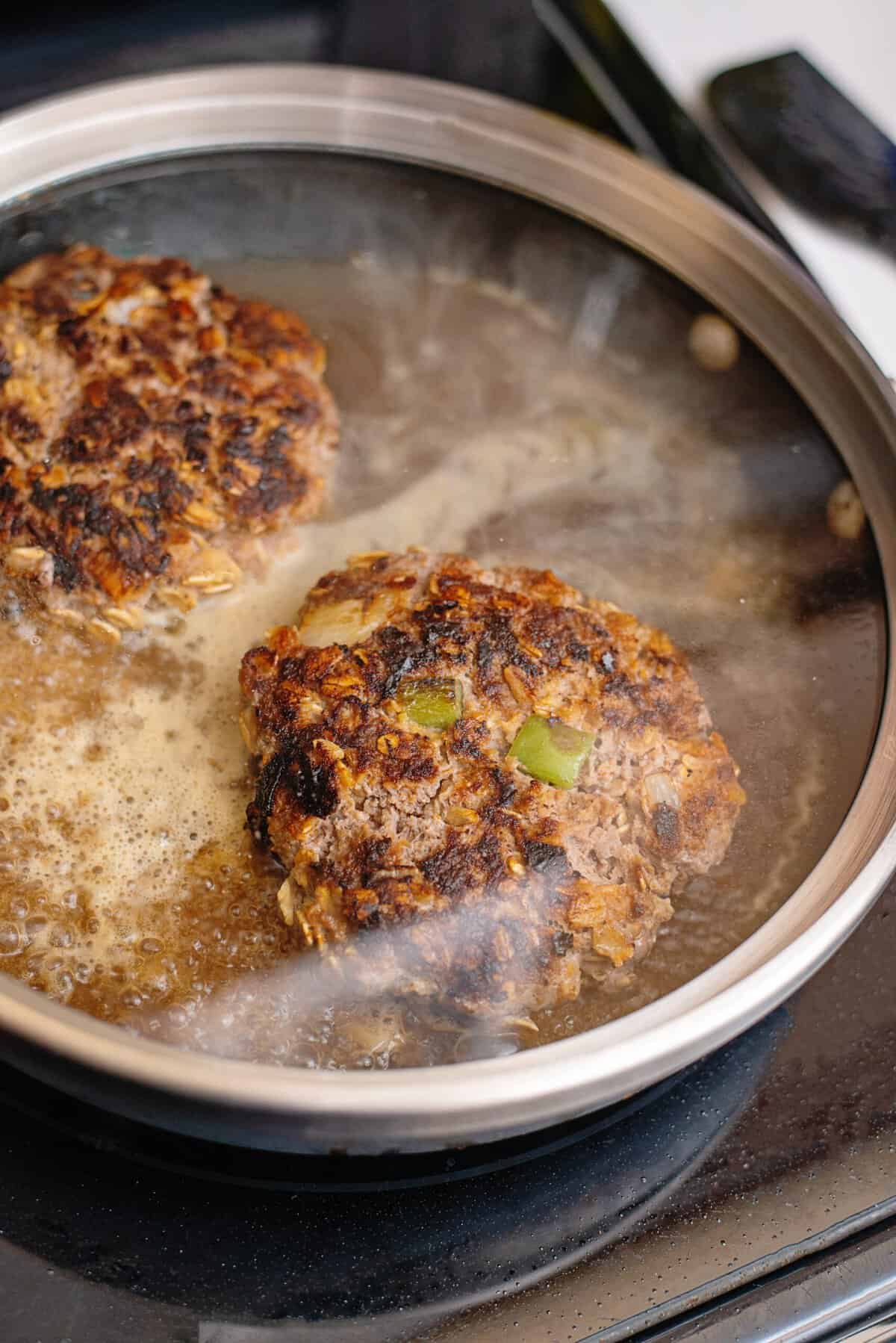 Meatloaf patties with water in a pan covered with a glass lid.