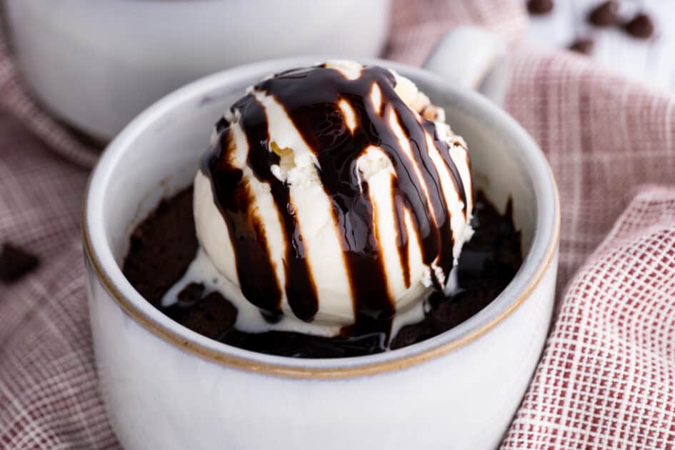 Microwave brownie in a mug with ice cream and chocolate syrup.