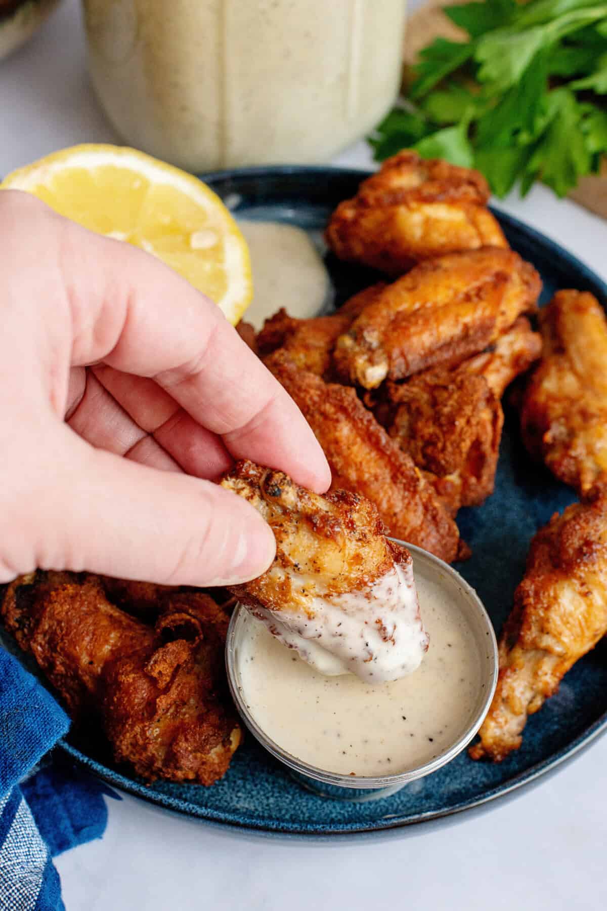 A hand dipping a chicken wing into Alabama white barbecue sauce.