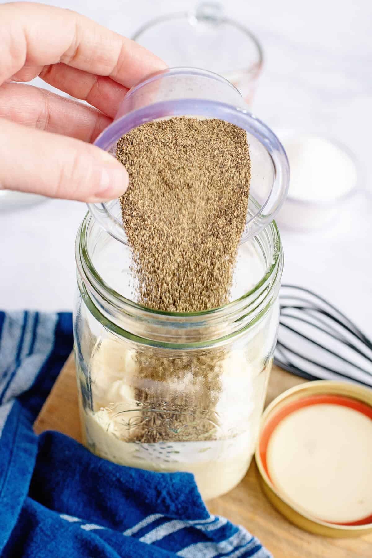 Adding black pepper to a mason jar.