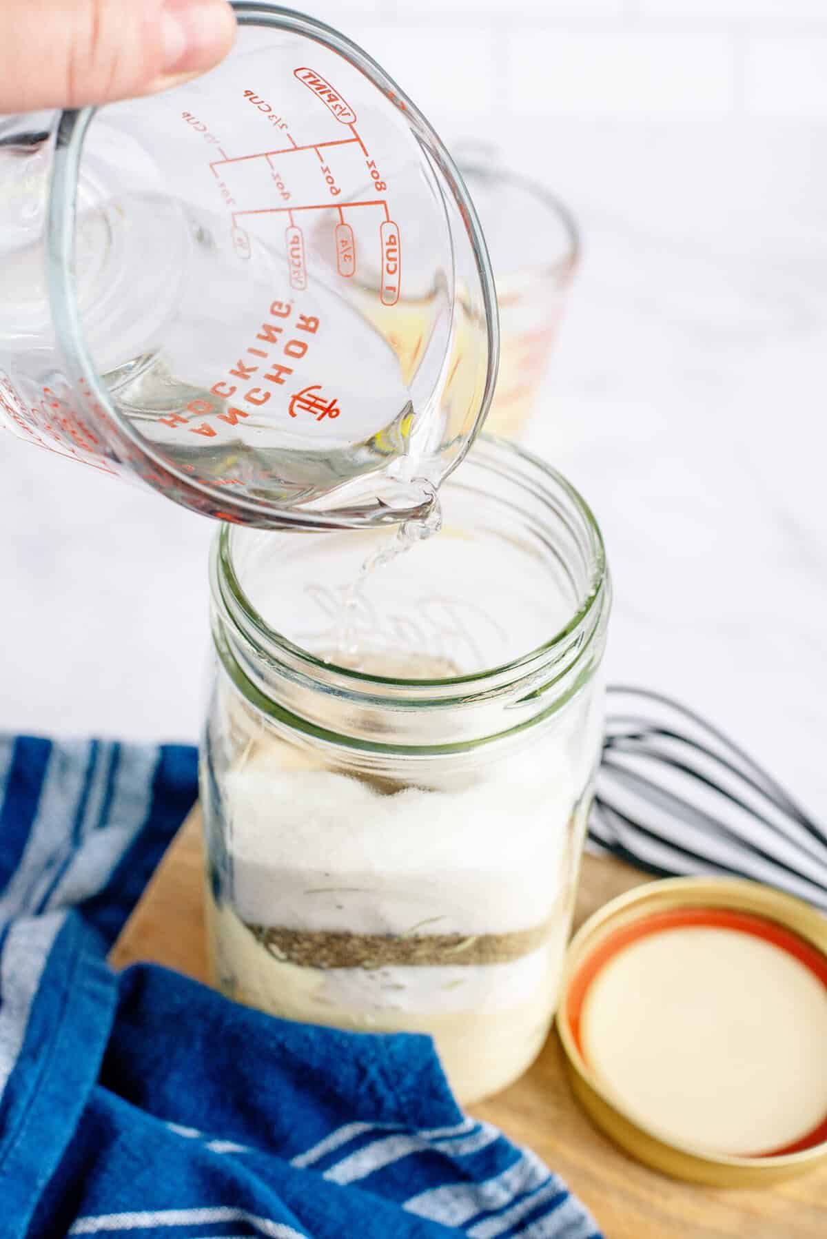 Adding white vinegar to a mason jar.