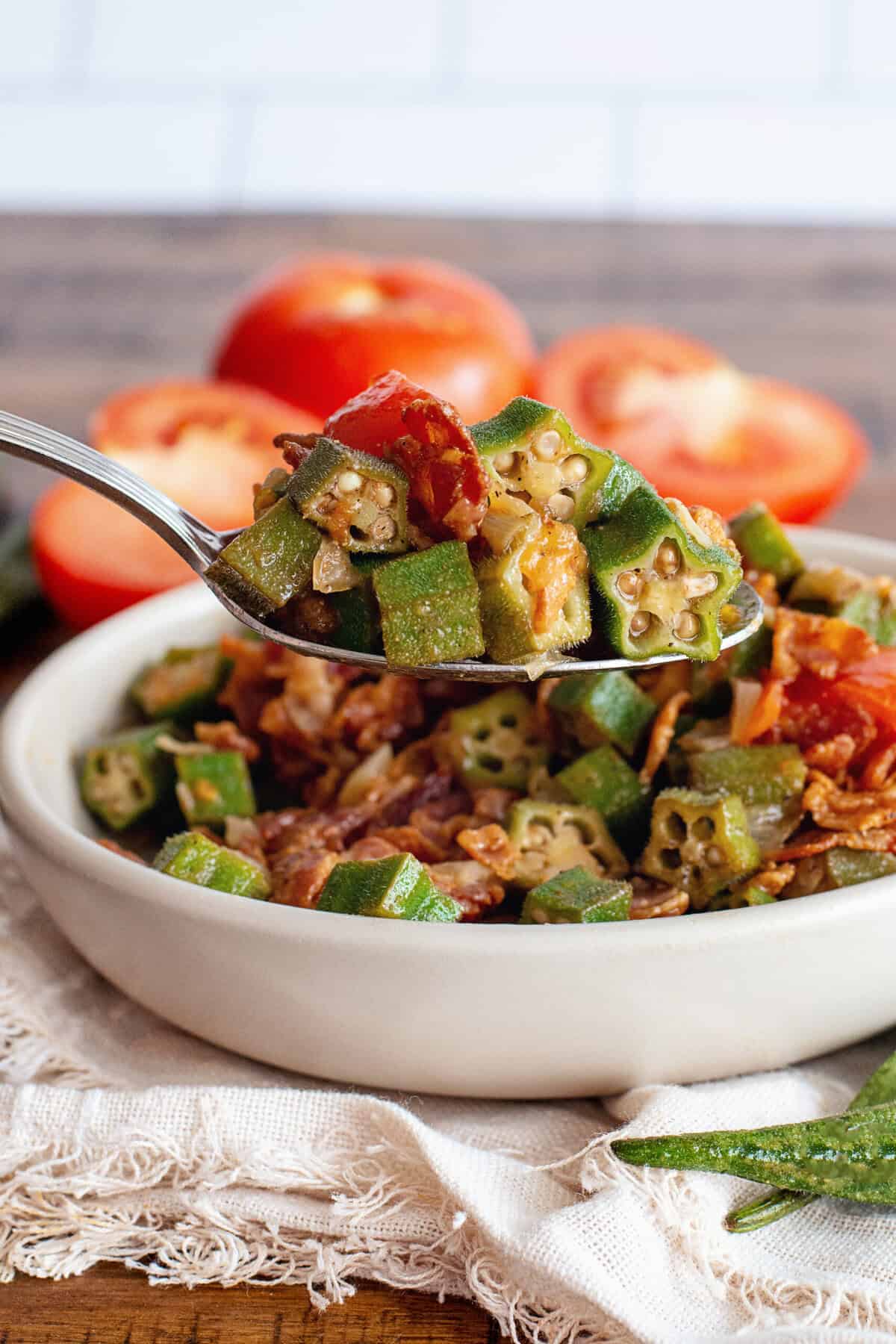 Steaming spoonful of okra and tomatoes with bacon, showing tender okra and chunky tomatoes in rich sauce.