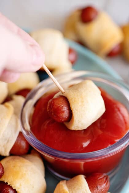 Dipping pigs in a blanket into ketchup.