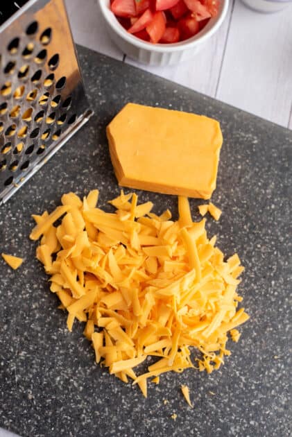 Freshly shredded cheddar cheese on chopping board.