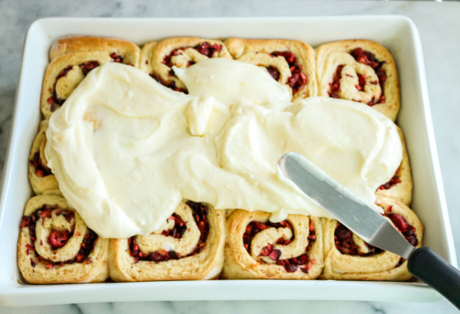 Spread cream cheese icing over baked cranberry orange rolls.