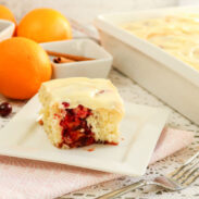 A cranberry orange roll in front of a baking dish filled with rolls.