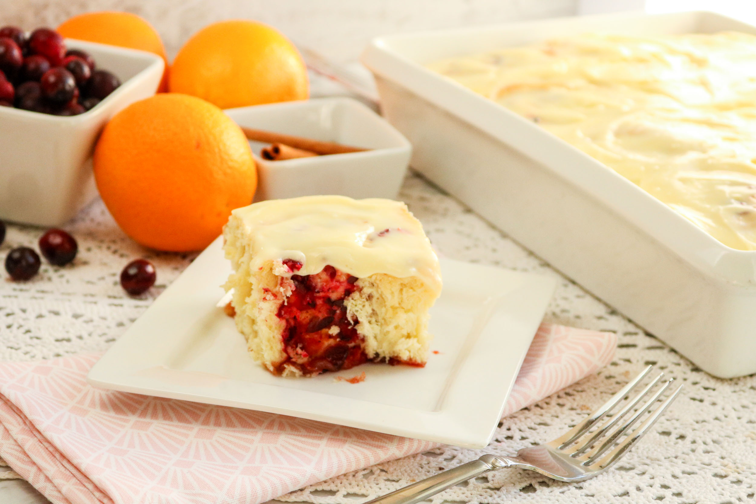 A cranberry orange roll in front of a baking dish filled with rolls.