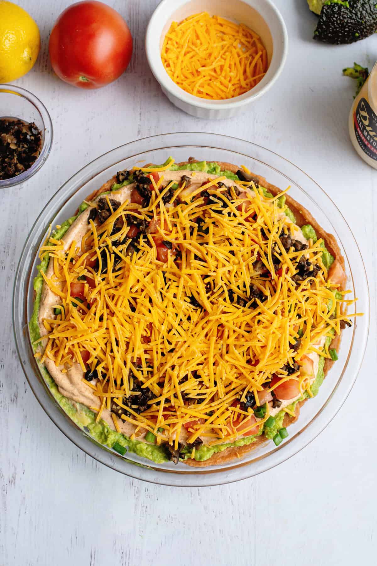 Tex Mex dip in a glass dish surrounded by ingredients.