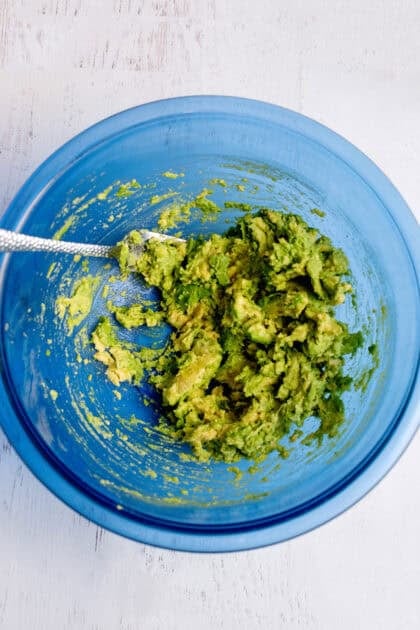 Mashed avocado in a glass blue bowl.