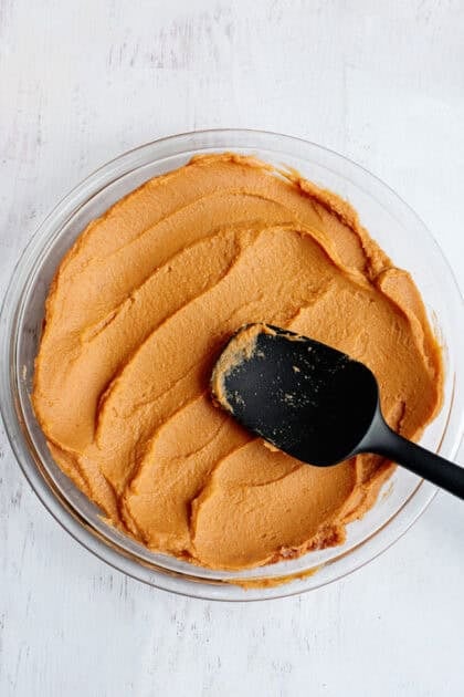 A black spatula spreading bean dip to the bottom of a glass dish.