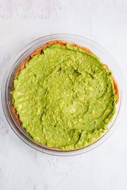 Guacamole spread on a layer of bean dip in a glass dish.
