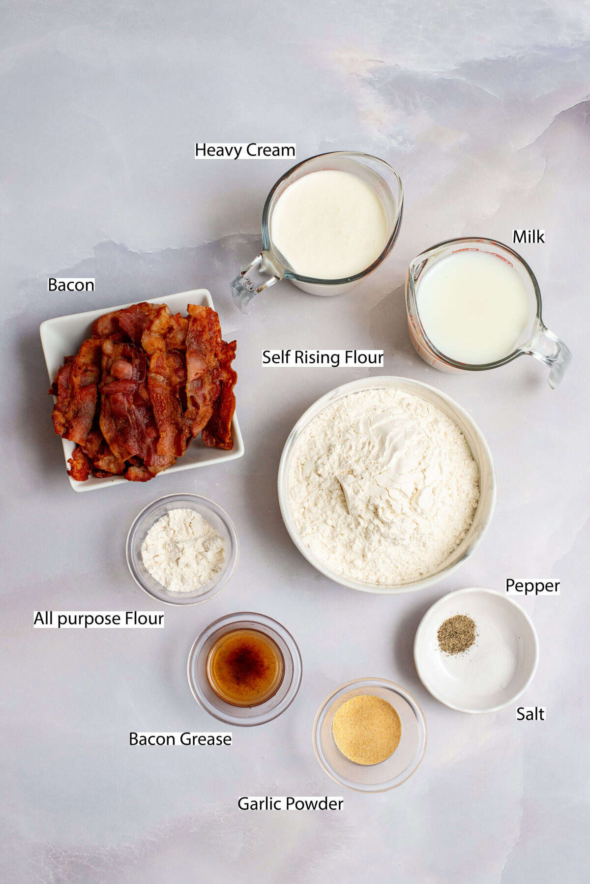 Ingredients for garlic biscuits and bacon gravy on a marble surface with labels.