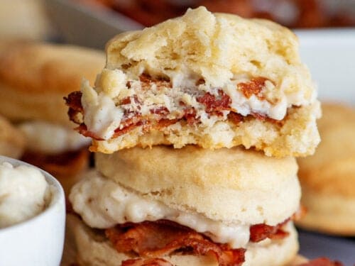 Stacked biscuits and bacon gravy with a bite out of the top biscuit.