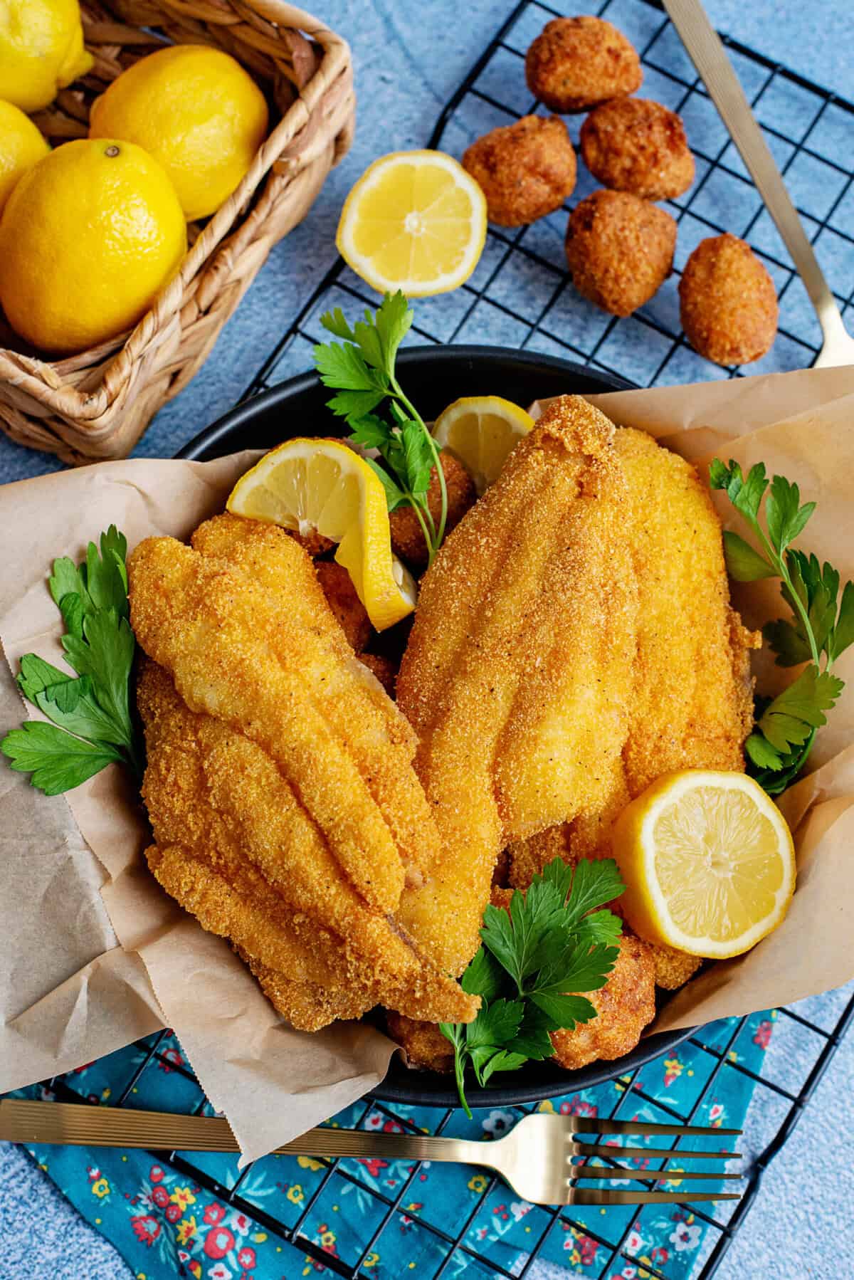 Southern fried catfish in a black bowl with lemon wedges and parsley.
